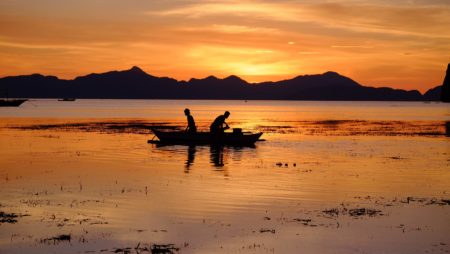 Silhoutte of two people on a boat in a lake against the sunset.