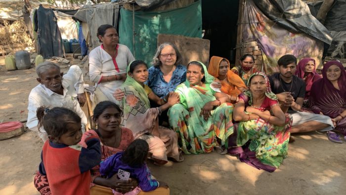 Gita Gill sitting with local women and men outdoors in front of a tent.