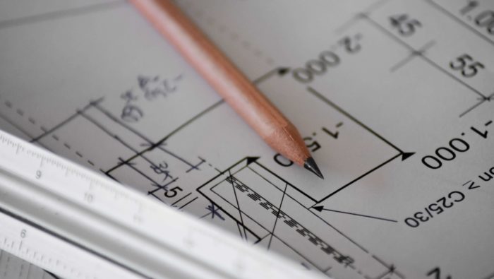 A brown pencil resting on a stack of building blueprints