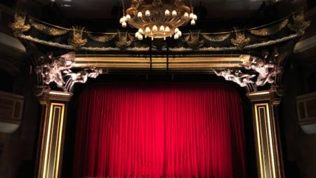 An empty grand theatre stage with the red curtains drawn closed.