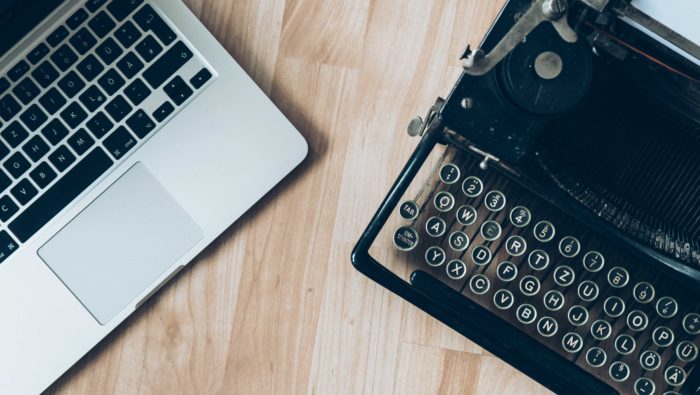 A modern laptop computer and a vintage typewriter on a wooden table.