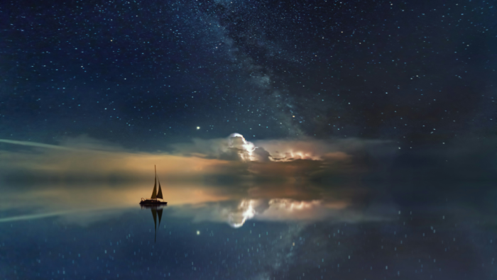 A small sailboat floats somewhere between sea and the night sky