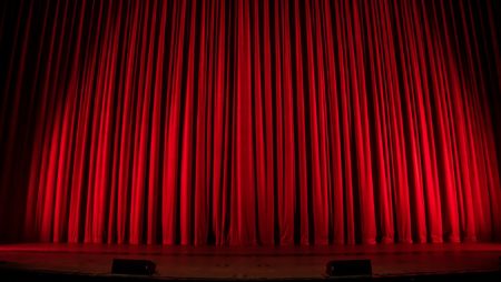 Thick red velvet curtains, lit up with stage lights at a theatre