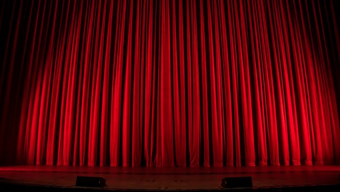 Thick red velvet curtains, lit up with stage lights at a theatre