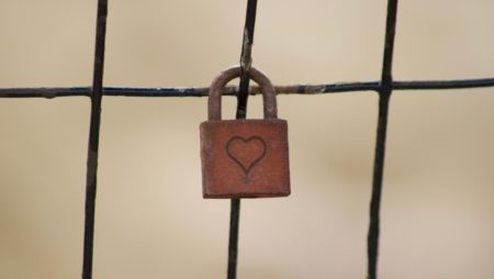 A photograph shows a rusted padlock - ethced with a heart - attached to a fence.