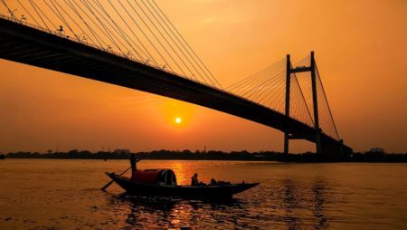 Sunset in West Bengal, a small boat passes under a vast bridge.