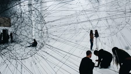 A group of people connecting threads in an art gallery space.