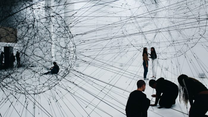 A group of people connecting threads in an art gallery space.