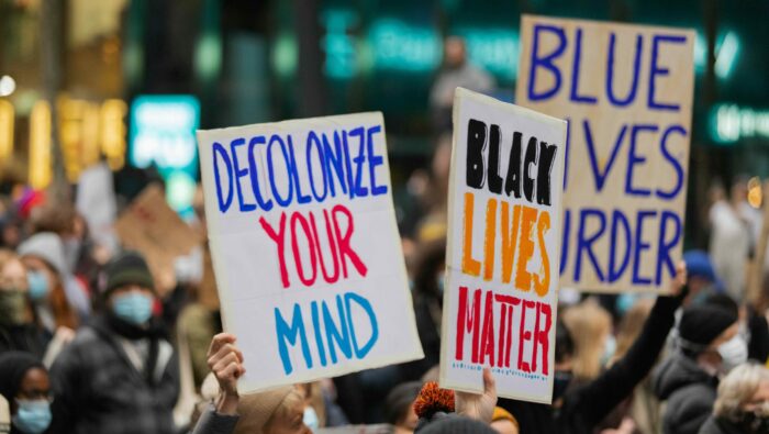 A picture from a protest with two signs saying "decolonize your mind" and "black lives matter"