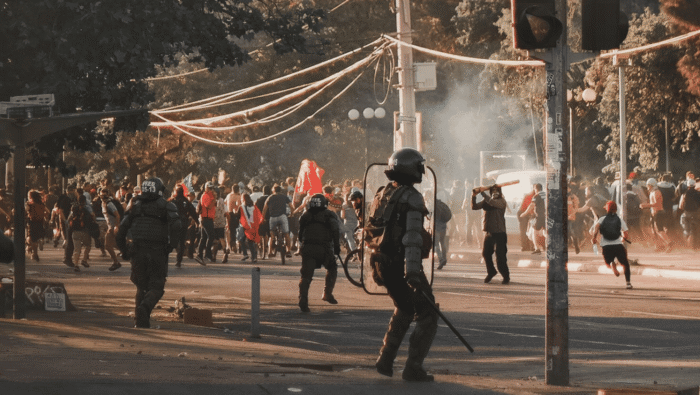 Picture of protestors and police officers, smoke in the background